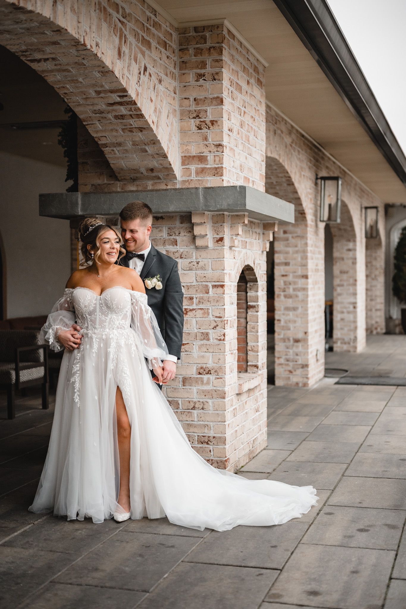 An elegant wedding portrait against rustic brick archways featuring a stunning off-shoulder gown.