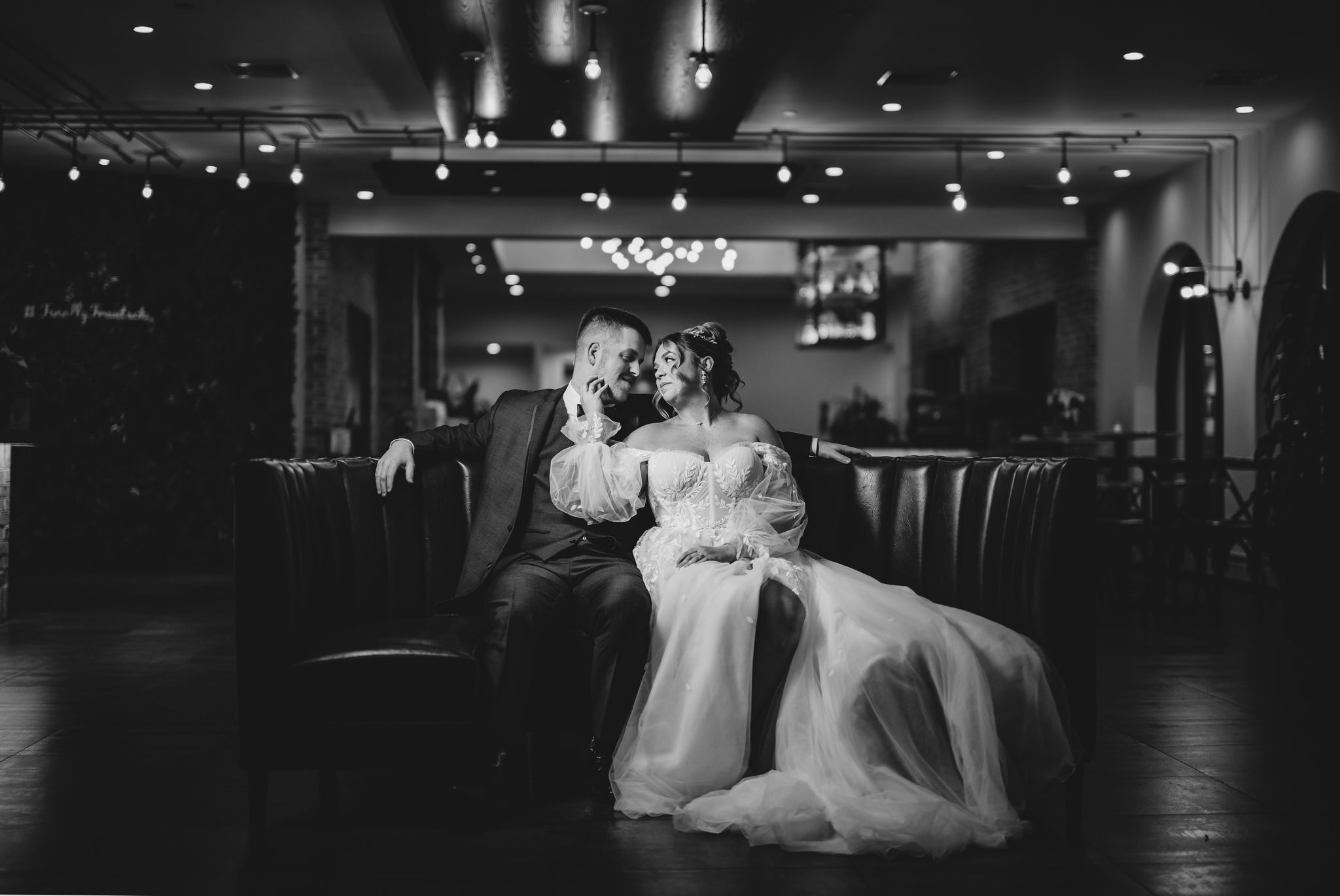 A romantic black and white wedding photo in an elegant reception venue with dramatic lighting.
