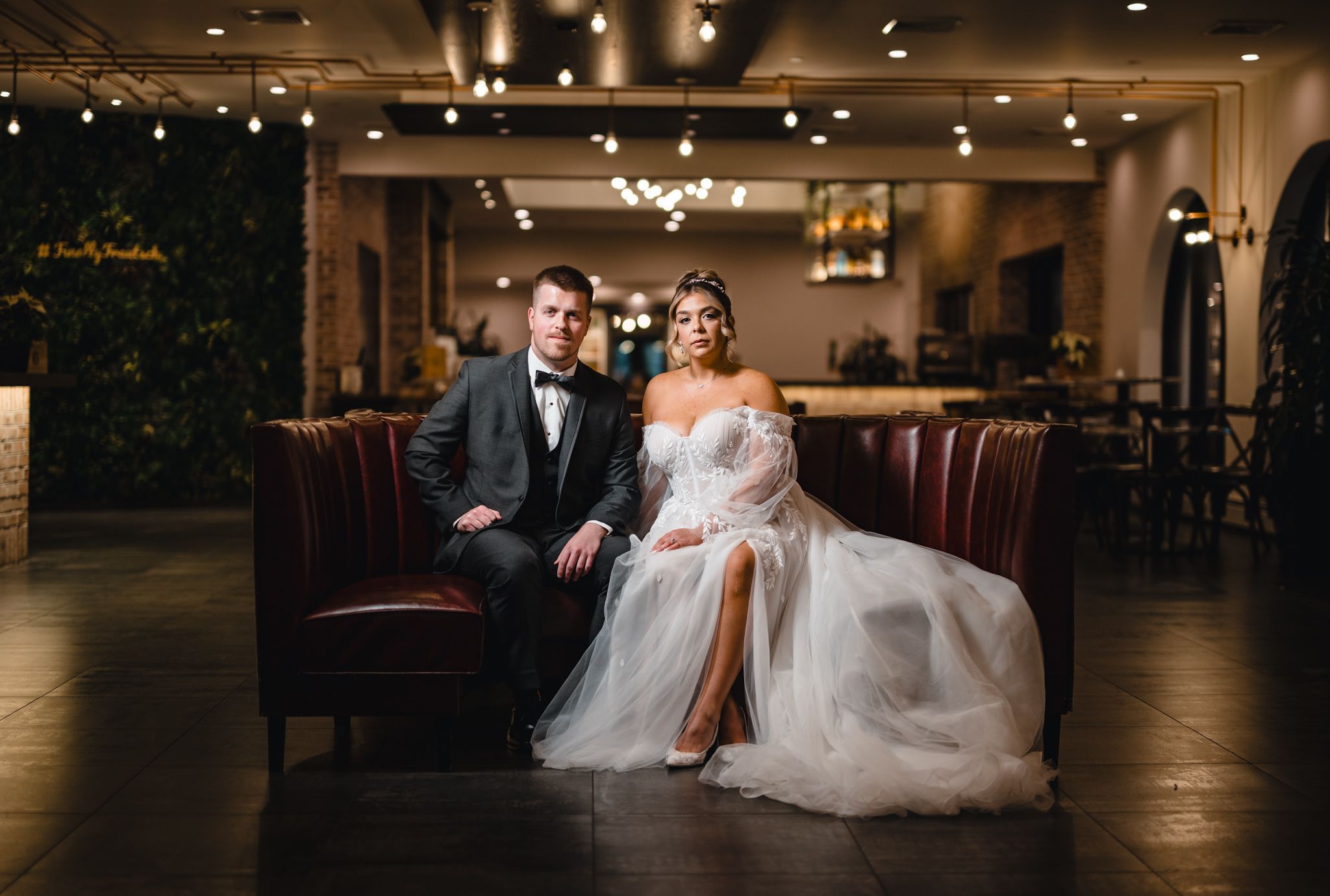 An elegant wedding photo in a modern venue with leather seating and mood lighting.