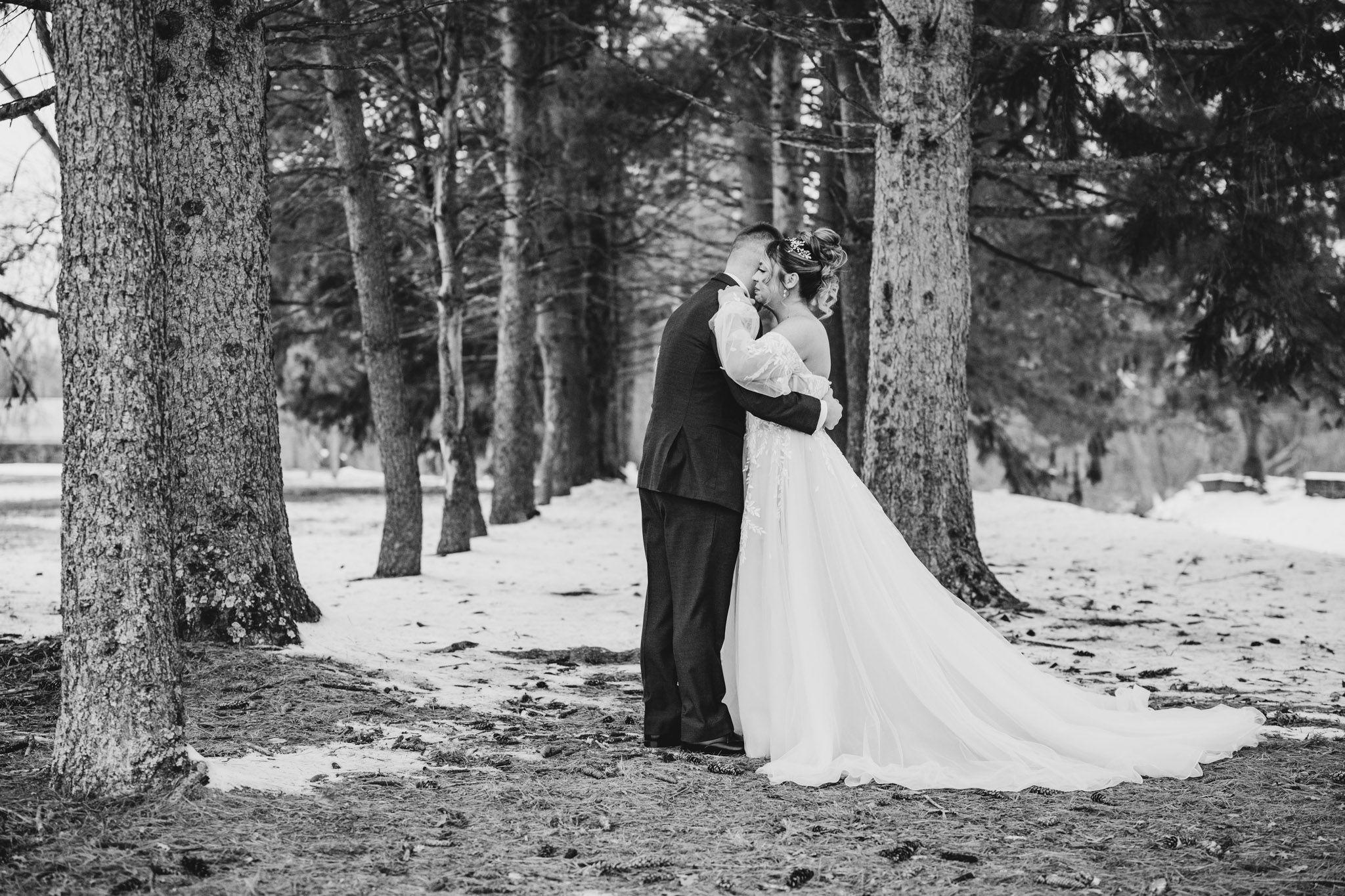 Romantic winter wedding photos captured among tall trees with snow on ground.