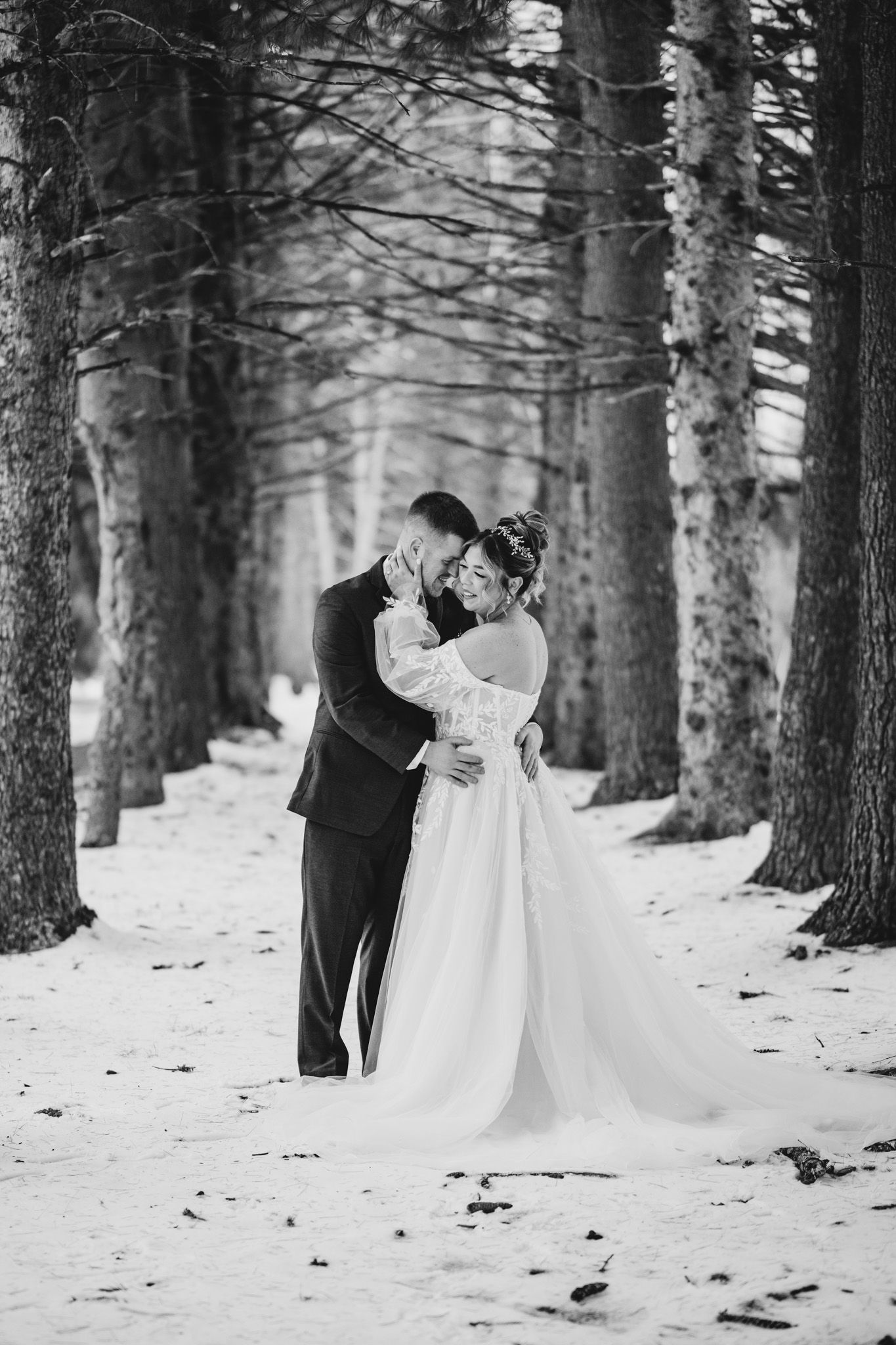 Black and white photo of wedding couple in snowy forest setting.