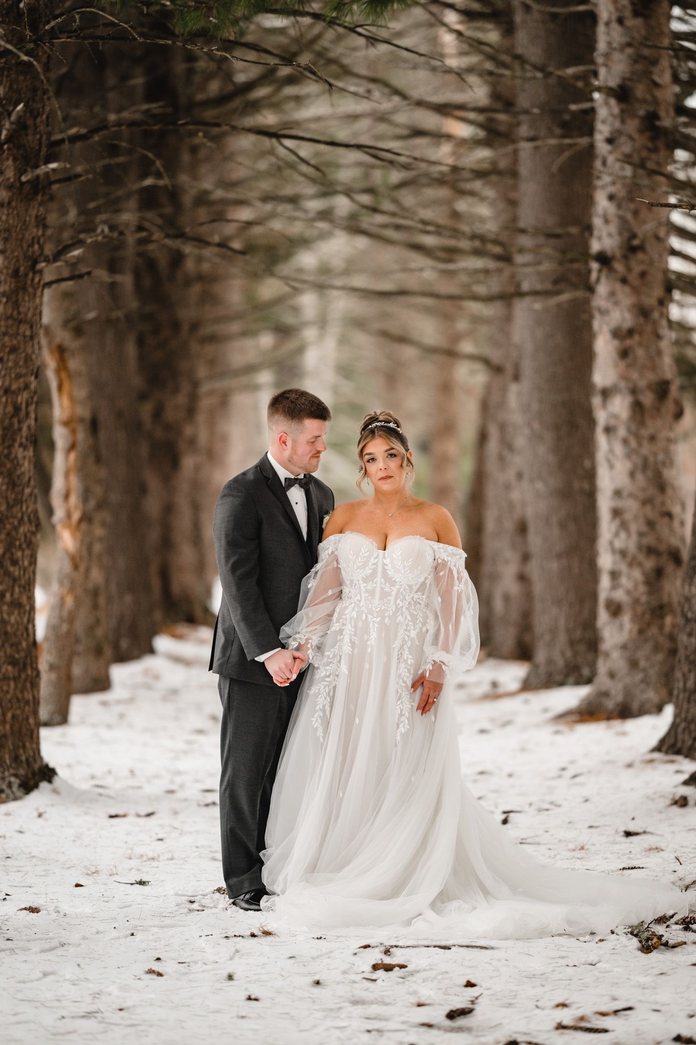 Elegant wedding couple walks through snow-covered pine forest.
