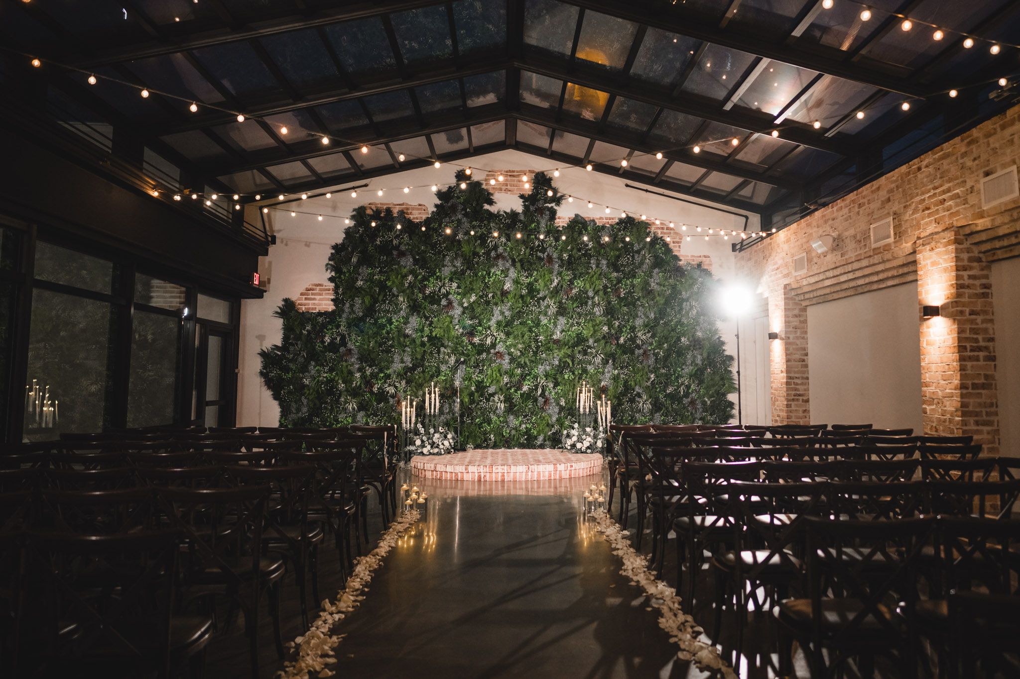An indoor wedding ceremony space with greenery arch and string lights creating romantic ambiance.
