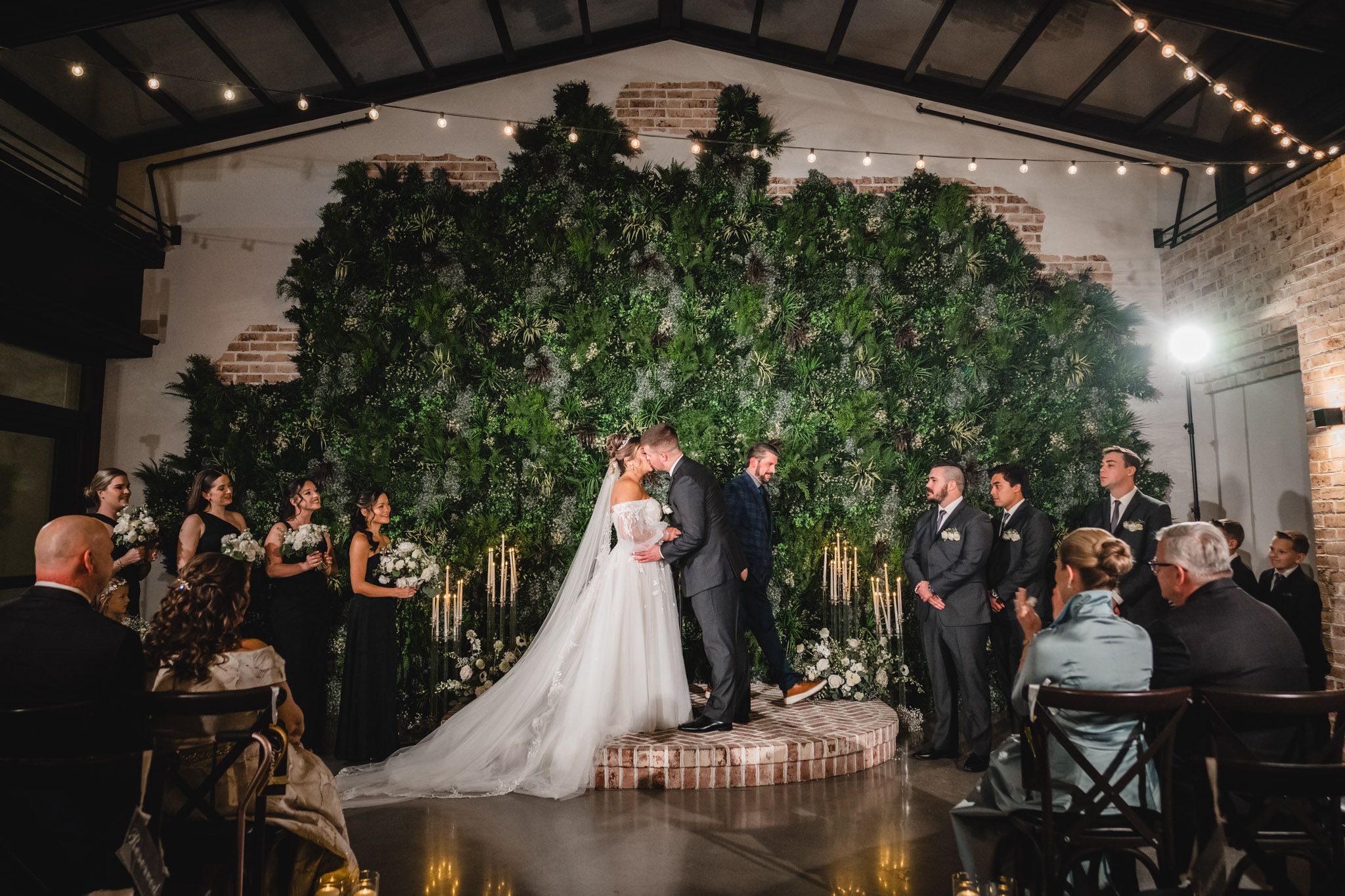 A wedding ceremony setup with a dramatic green wall backdrop and string lights in an indoor venue.