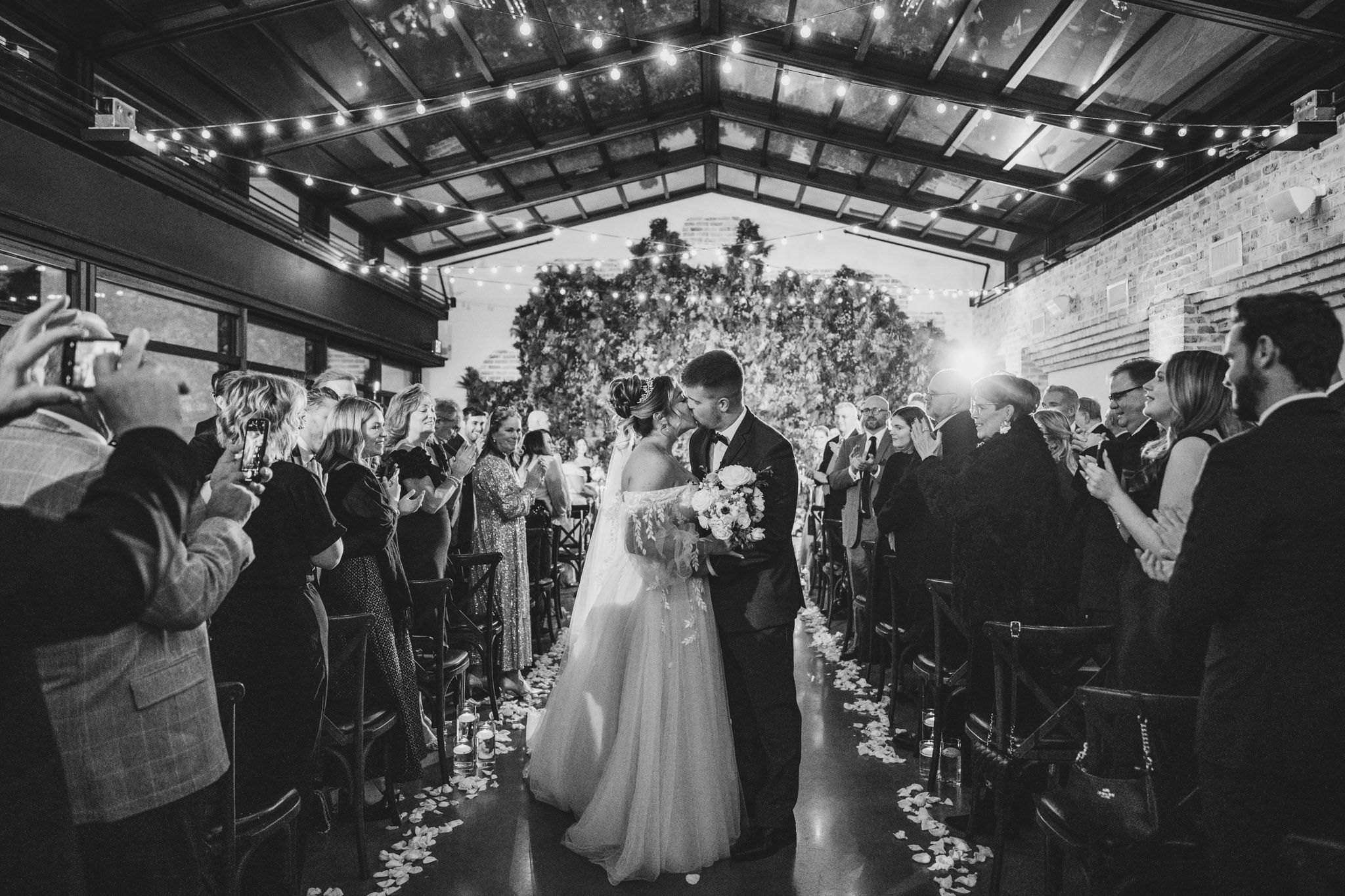 A black and white photo of a couple's first dance with guests holding sparklers in an indoor venue.