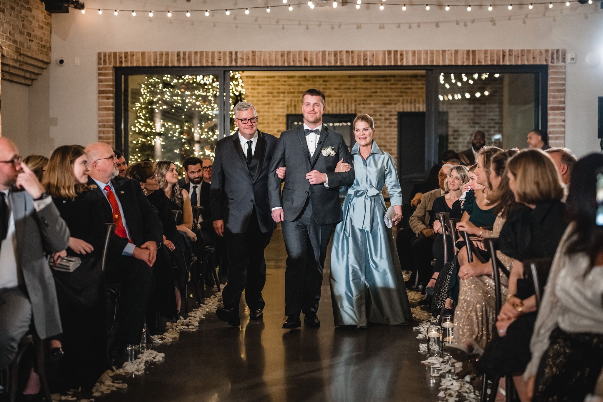 A wedding processional in an industrial-style venue with exposed brick and string lights.
