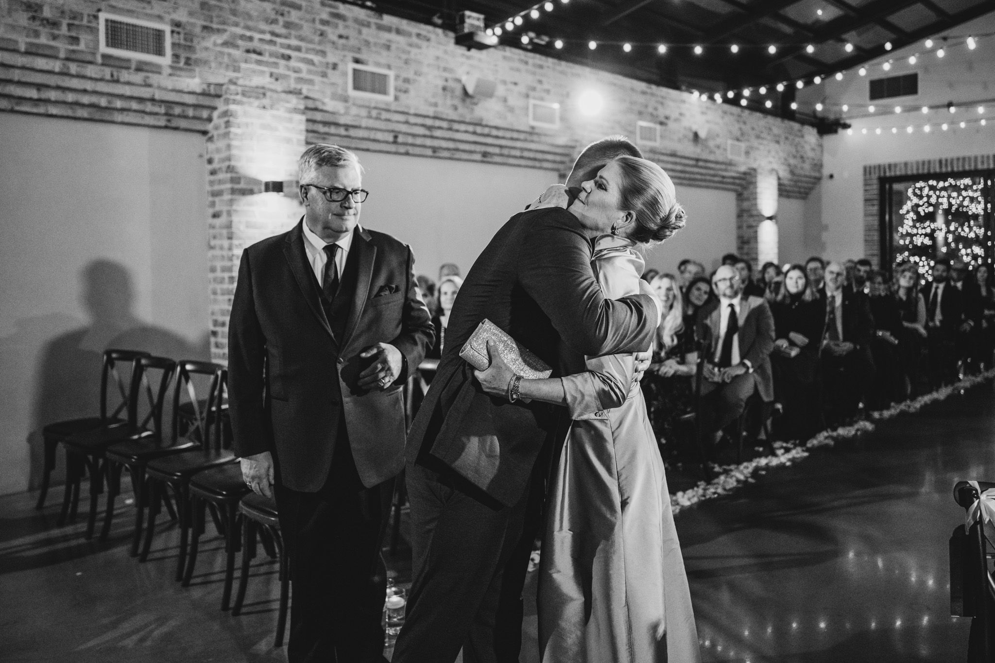 A tender black and white wedding moment captured in an industrial venue with string lights.
