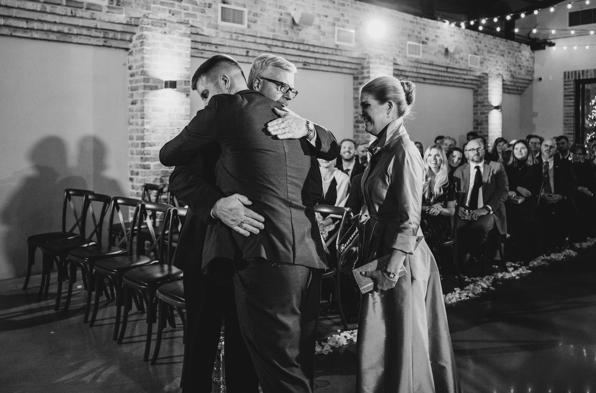 A black and white emotional moment during a wedding ceremony in a brick-walled venue.