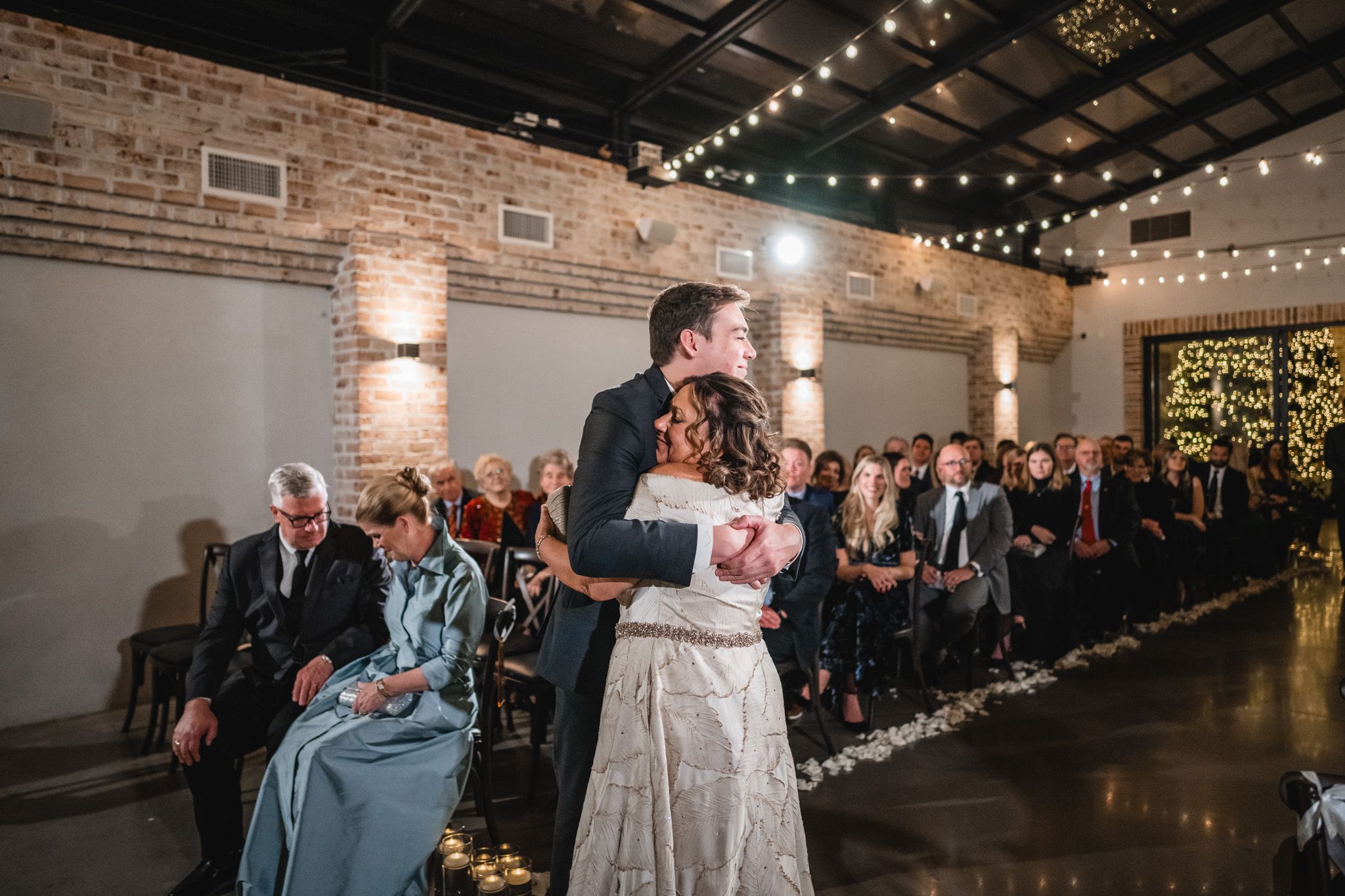 A couple shares their first dance in an industrial-chic venue with exposed brick walls and string lights overhead.