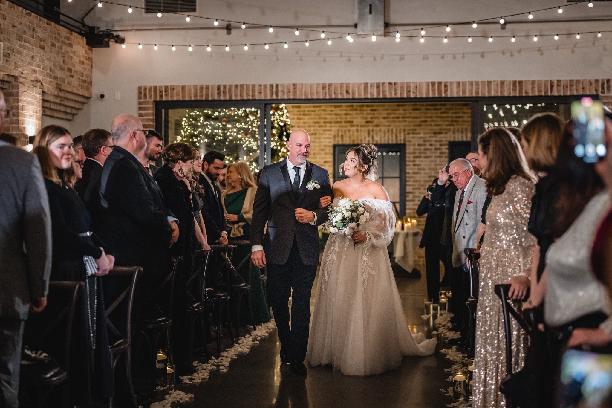 A wedding ceremony in a modern brick venue with string lights and floral decorations.