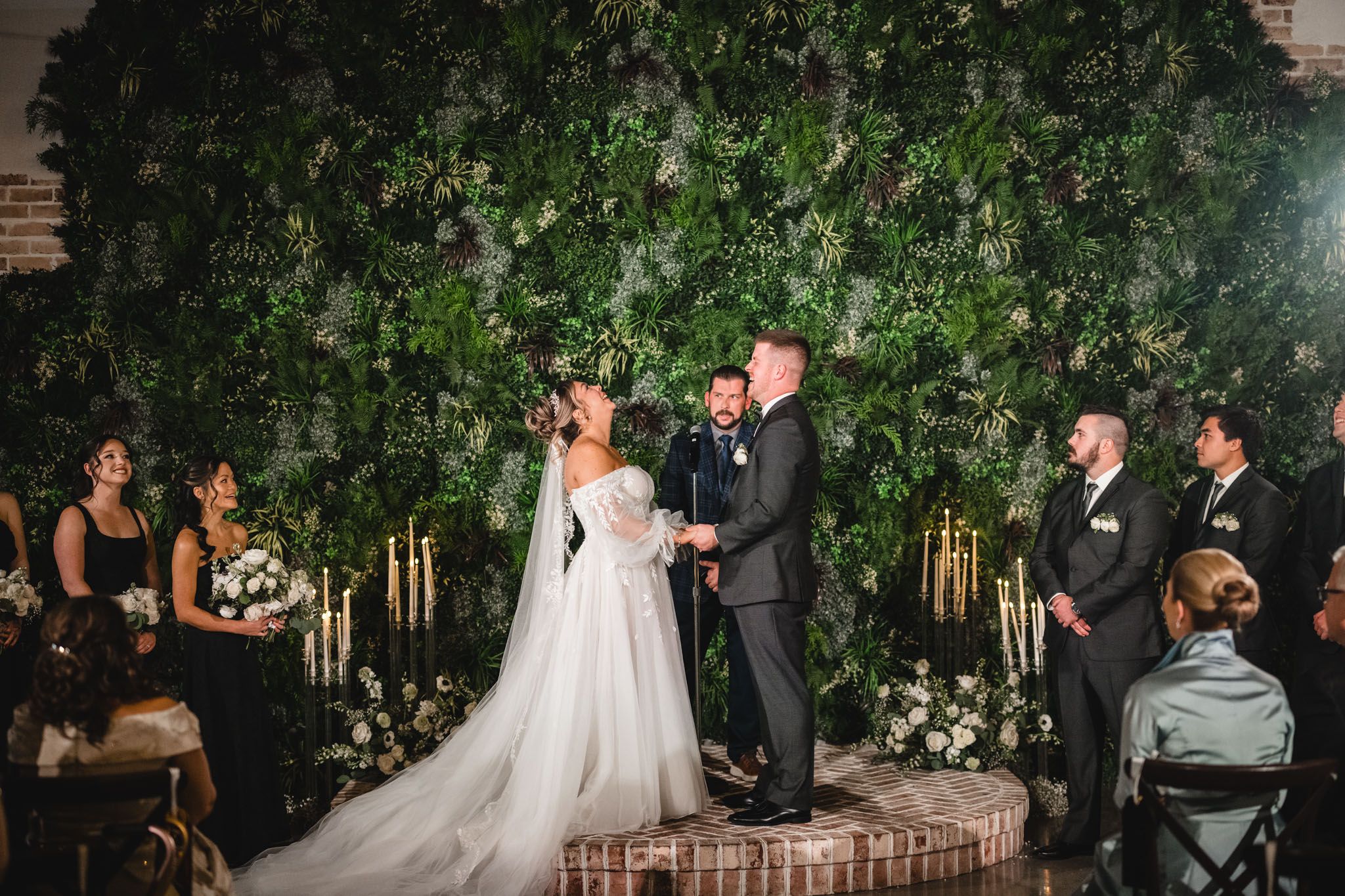 A ceremony taking place in front of a lush greenery wall with glowing candles.