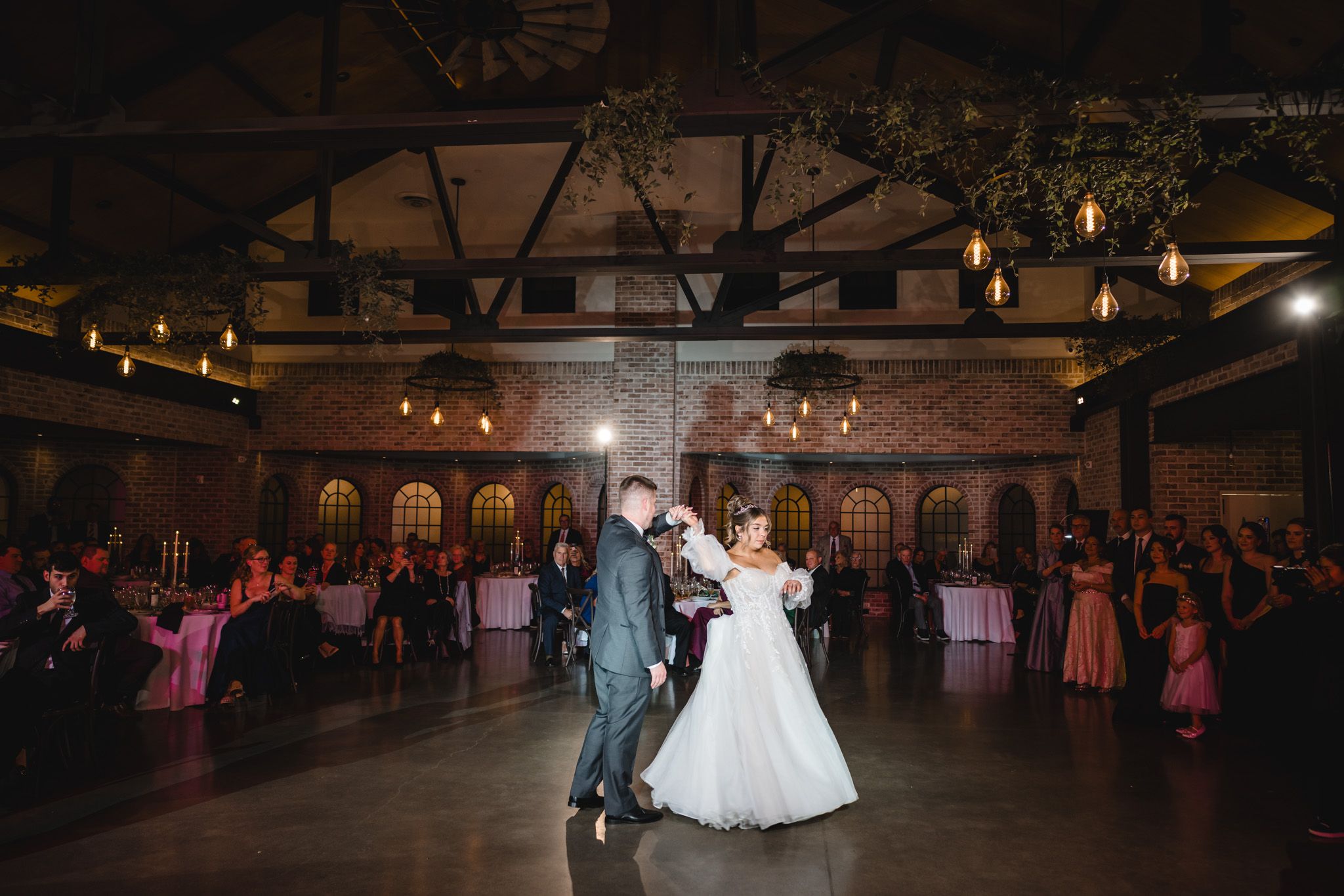 Wedding reception dance floor scene with dramatic lighting in a rustic indoor venue.