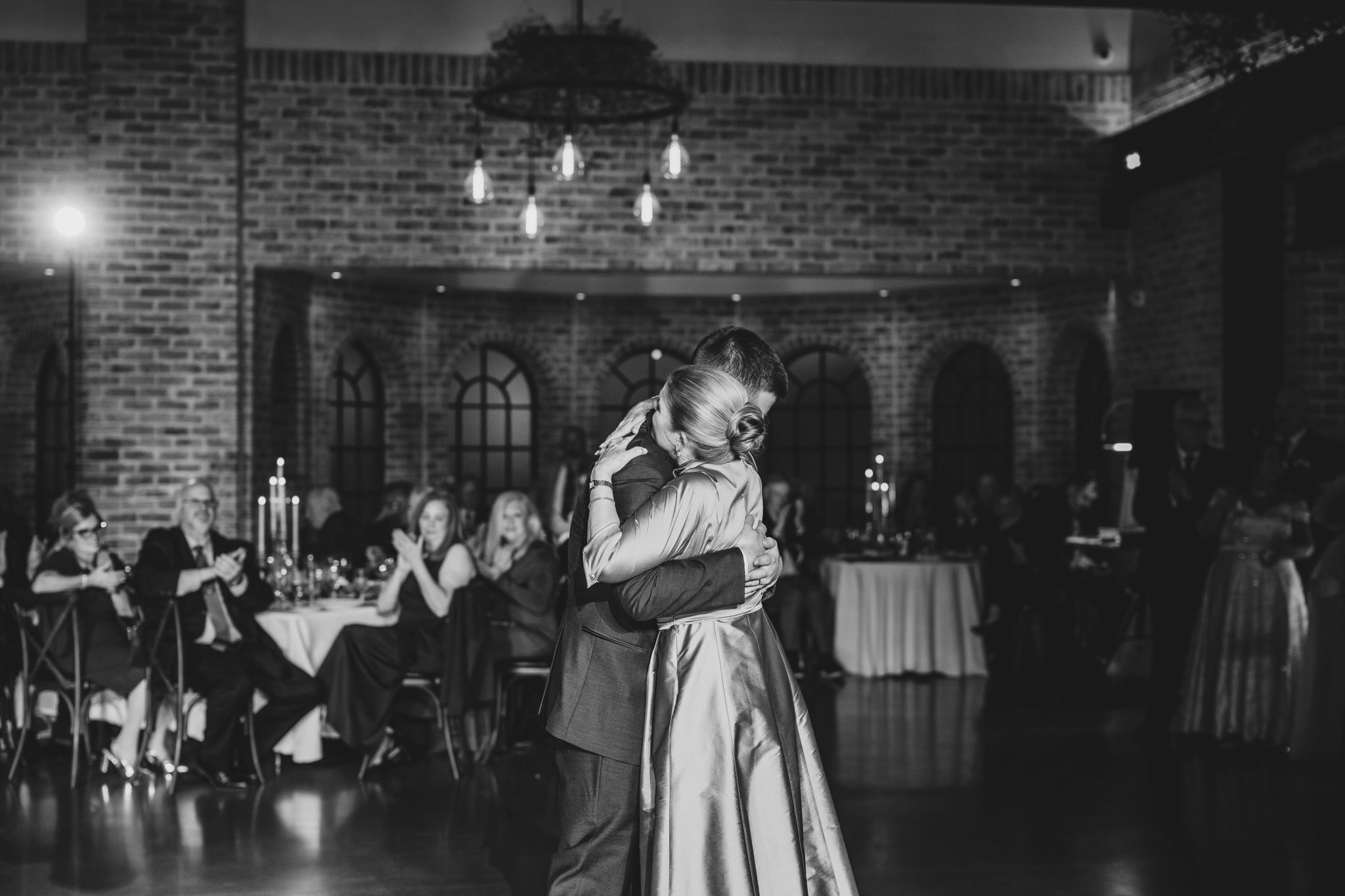 A black and white photo of a romantic slow dance in a rustic brick venue.