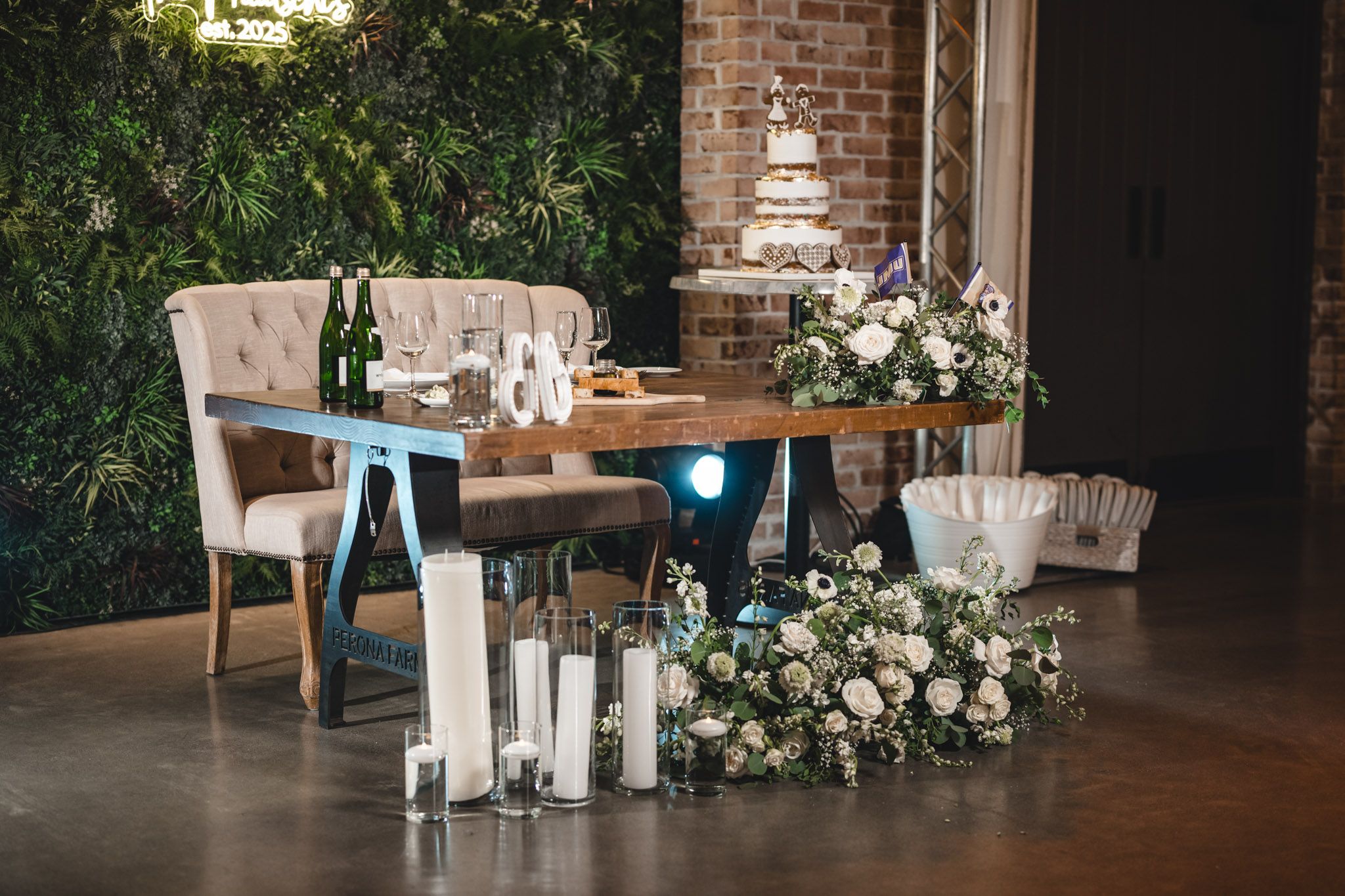 An elegant sweetheart table setup with floral arrangements and blue accents against a greenery wall.