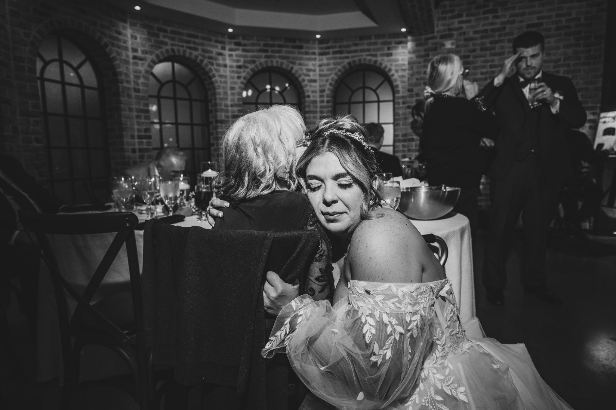 An intimate candid moment captured during a wedding reception in a brick-walled venue.
