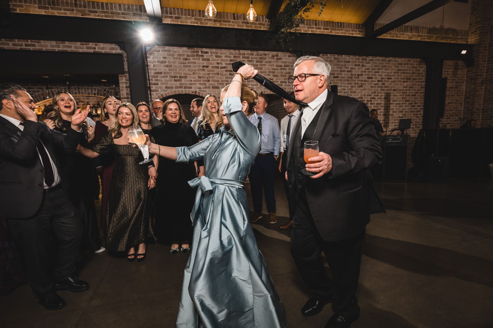Wedding guests dancing and celebrating in an industrial-style venue with exposed brick walls.