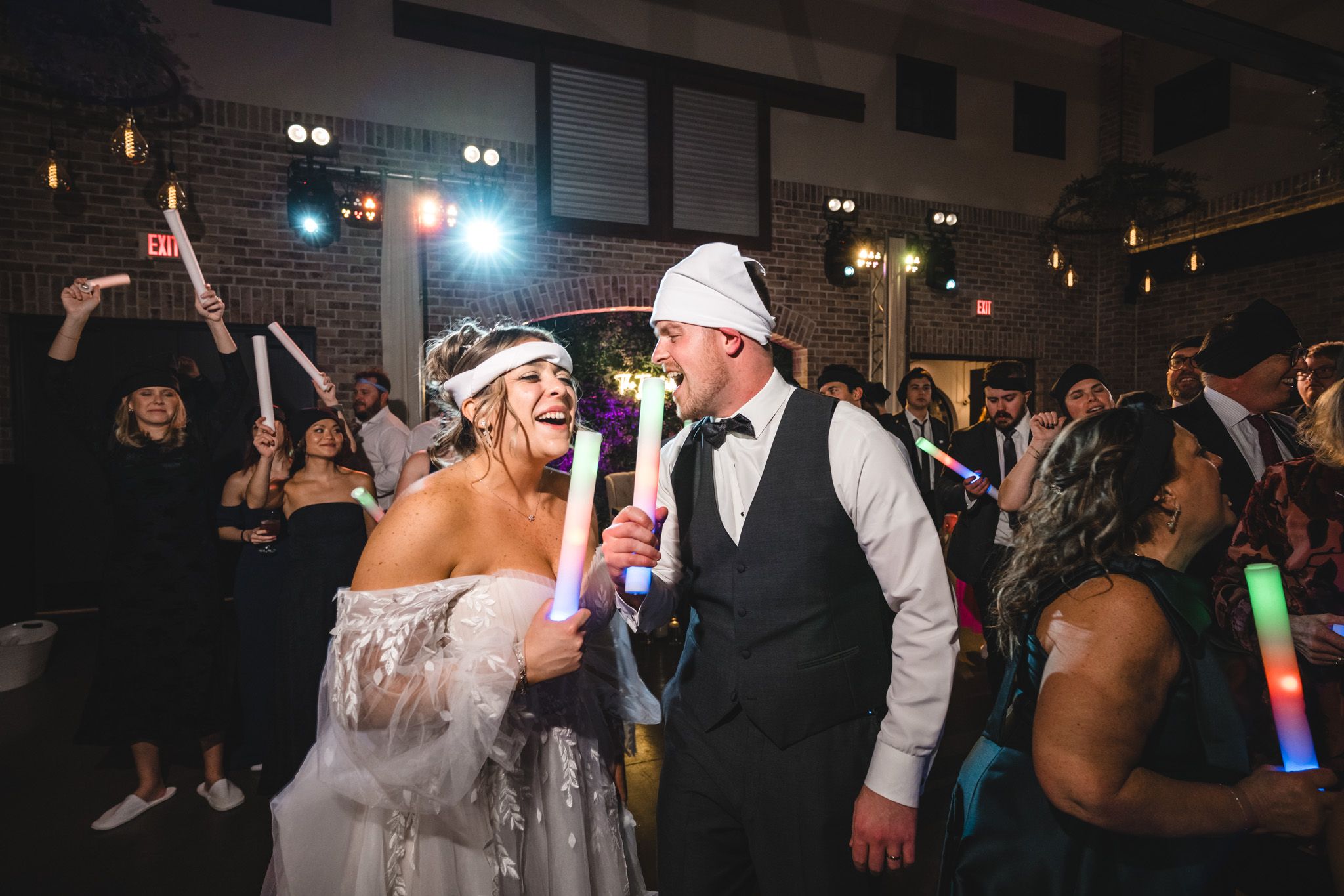 Wedding party members dancing with glow sticks during reception celebration.