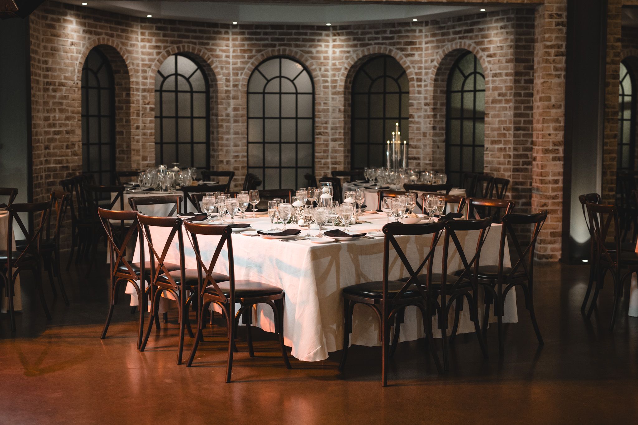 Elegant wedding reception venue with exposed brick walls, arched windows, and tables set for dining.