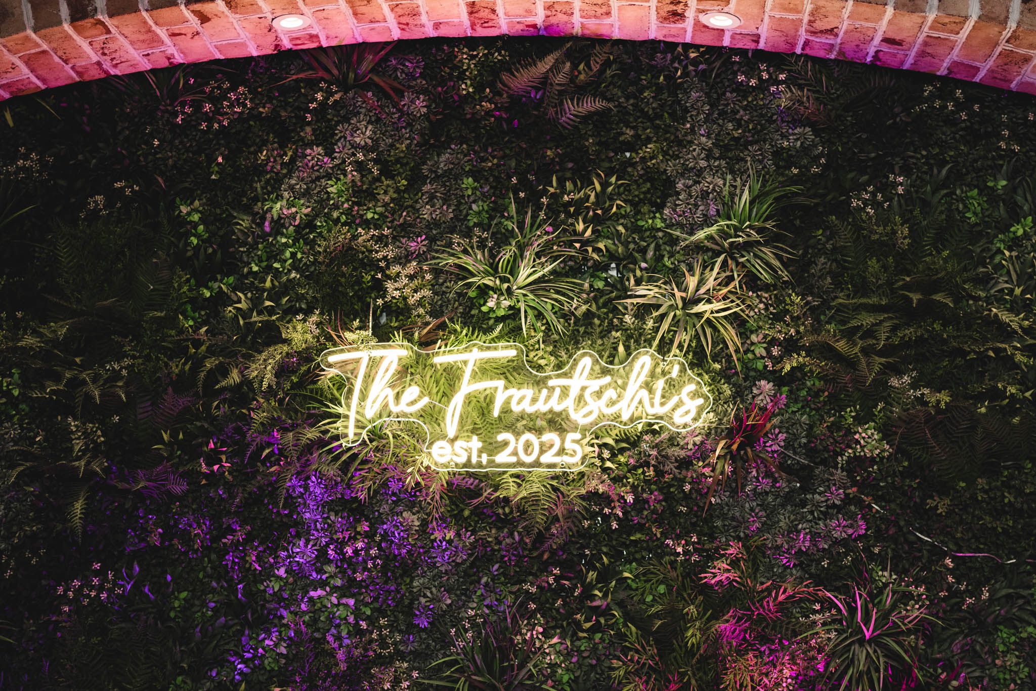 Outdoor wedding venue decorated with neon signage and purple floral arrangements.