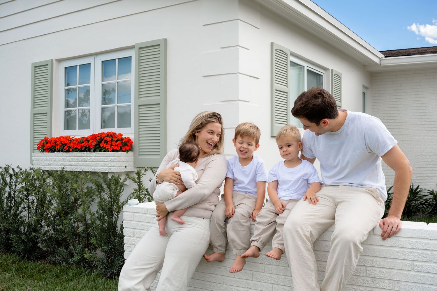 Family members wearing white outfits lounge together on a white couch for a casual home photoshoot.