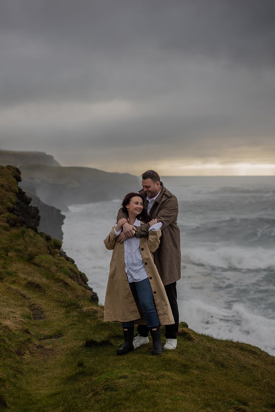 Adventure engagement session on Doolin cliffs with crashing waves and moody Irish sky
