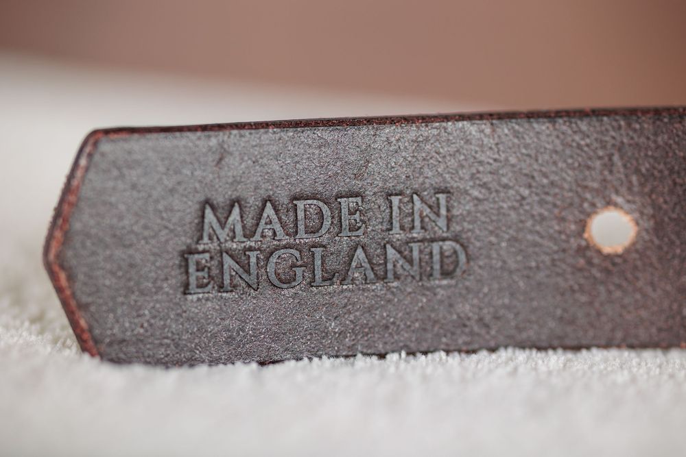 Close-up of a dark brown leather strap embossed with Made in England text, resting on a white surface.