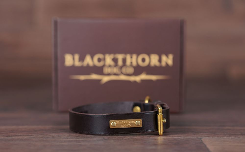 Black leather bracelet with gold hardware by Blackthorn Leag Co, displayed in front of branded burgundy gift box.