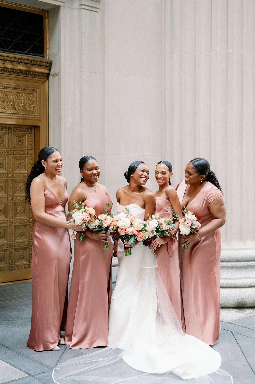 Wedding party in blush pink bridesmaid dresses and white bridal gown pose together in front of ornate door. - Fairlie Chicago Wedding