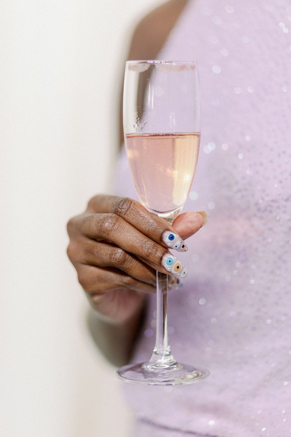 Hand holding a champagne glass filled with pink sparkling wine against a soft pink bokeh background. - Fairlie Chicago Wedding