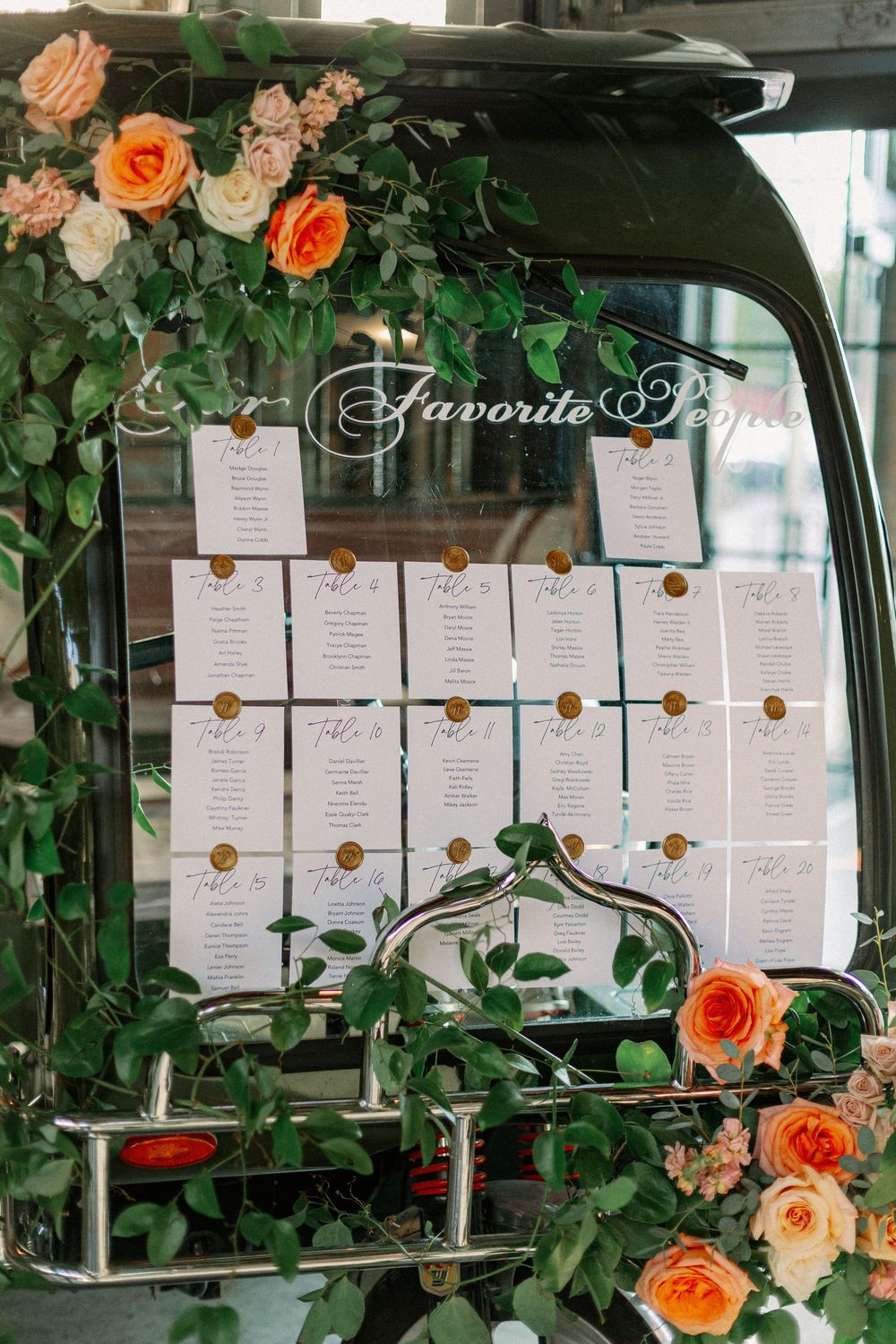 Wedding seating chart displayed on black vintage car window with orange roses and greenery decorations. - Fairlie Chicago Wedding