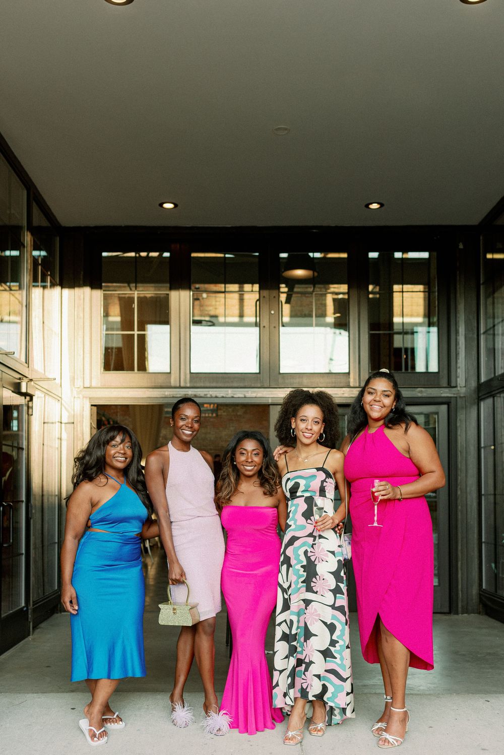 A group poses together in a modern building hallway wearing bright blue and pink dresses. - Fairlie Chicago Wedding