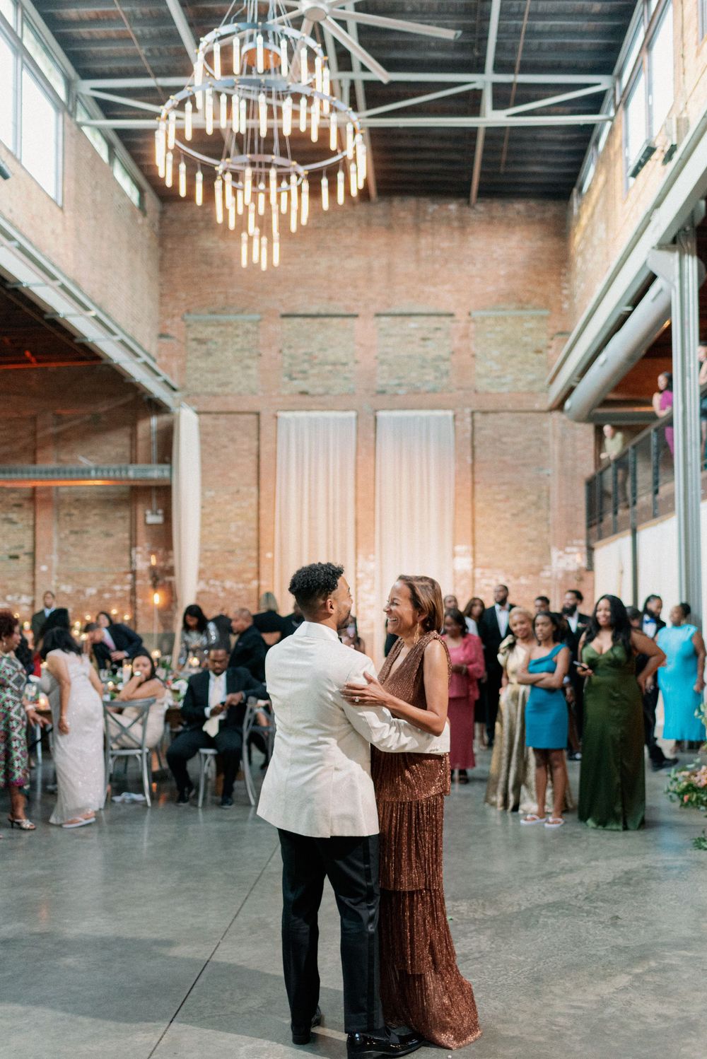 People dancing and socializing at an industrial-style event venue with exposed brick walls and elegant chandeliers. - Fairlie Chicago