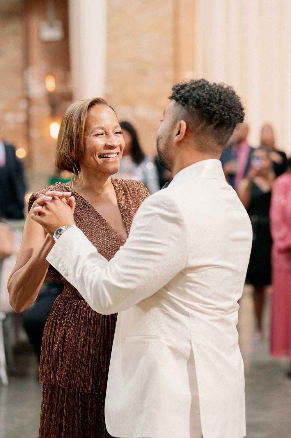 A couple dances and laughs together at an elegant event, with the woman wearing brown and man in white attire. - Fairlie Chicago Wedding