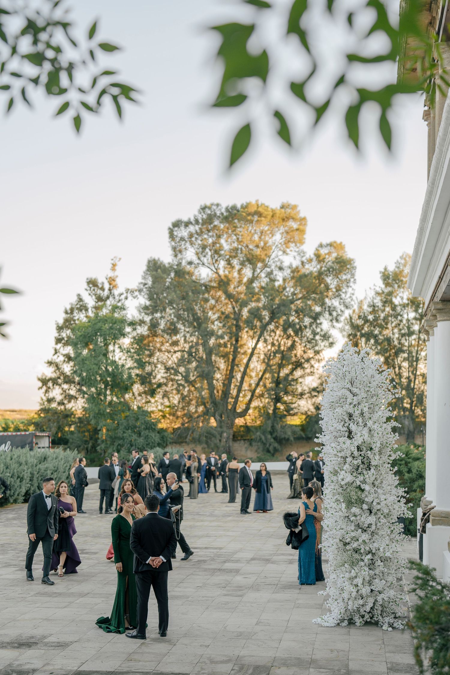Elegant outdoor wedding reception with floral decor and guests mingling on a stone patio at sunset.