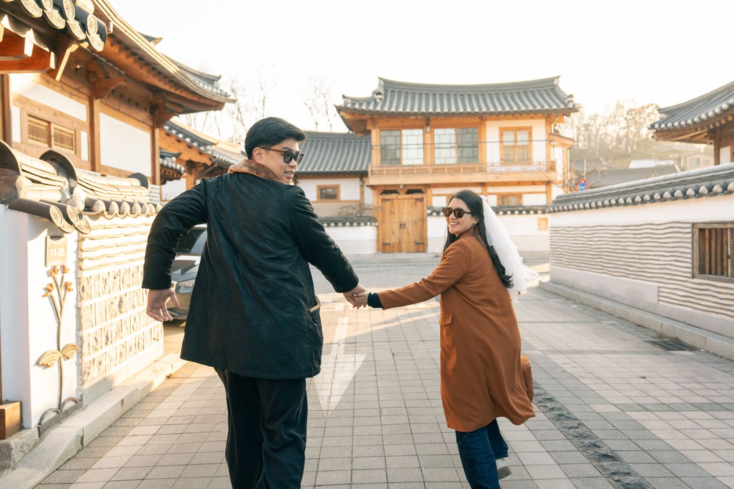 Two people walk and interact along a traditional Korean palace walkway with ornate wooden architecture.
