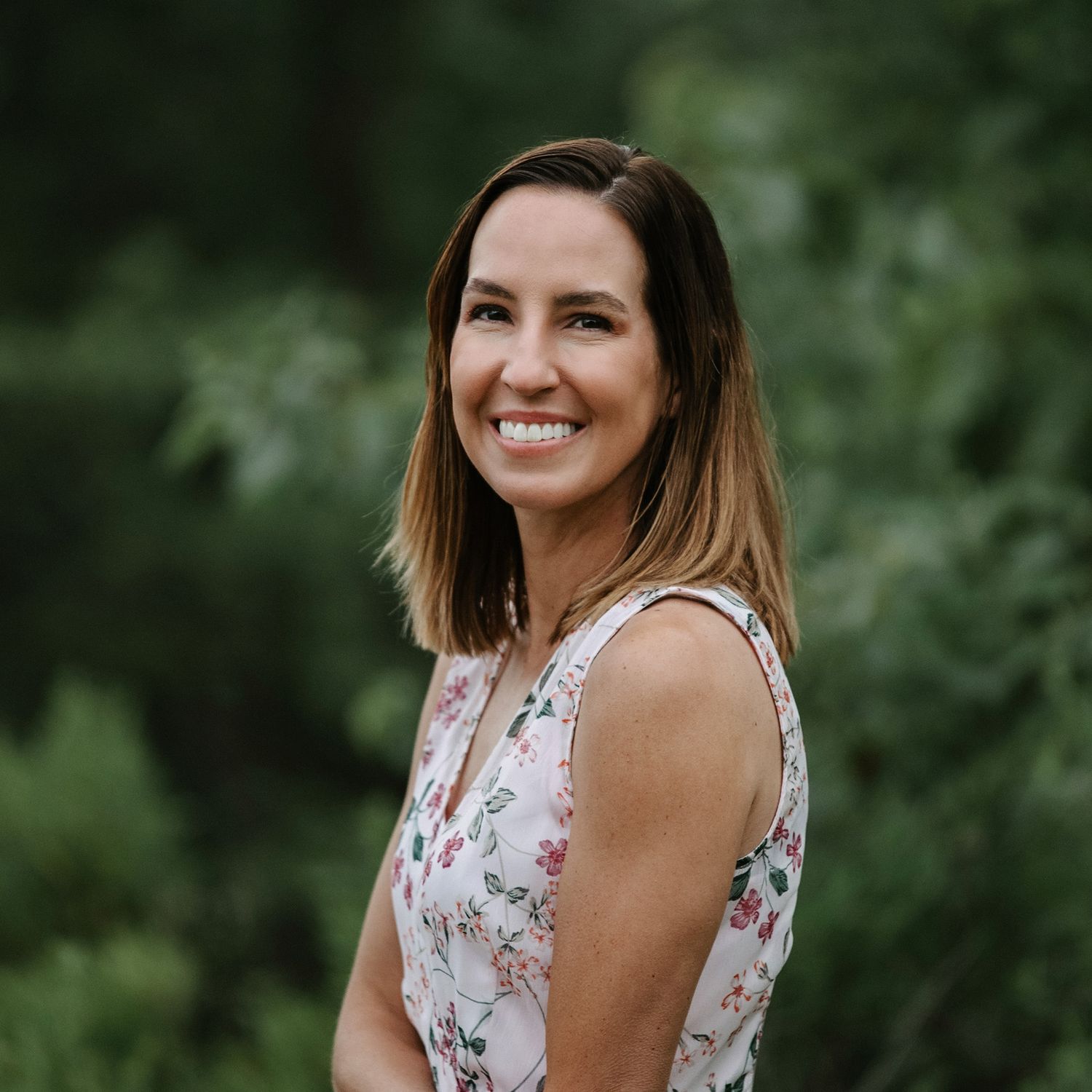 Professional headshot of woman smiling outdoors with soft natural background.