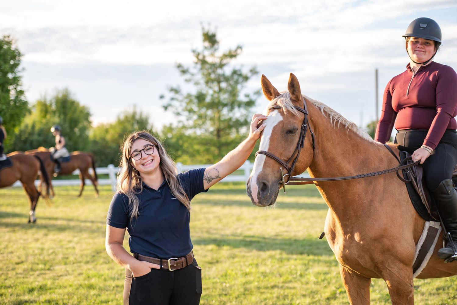 A chestnut horse stands in a sunny field during an outdoor riding lesson on a summer evening.