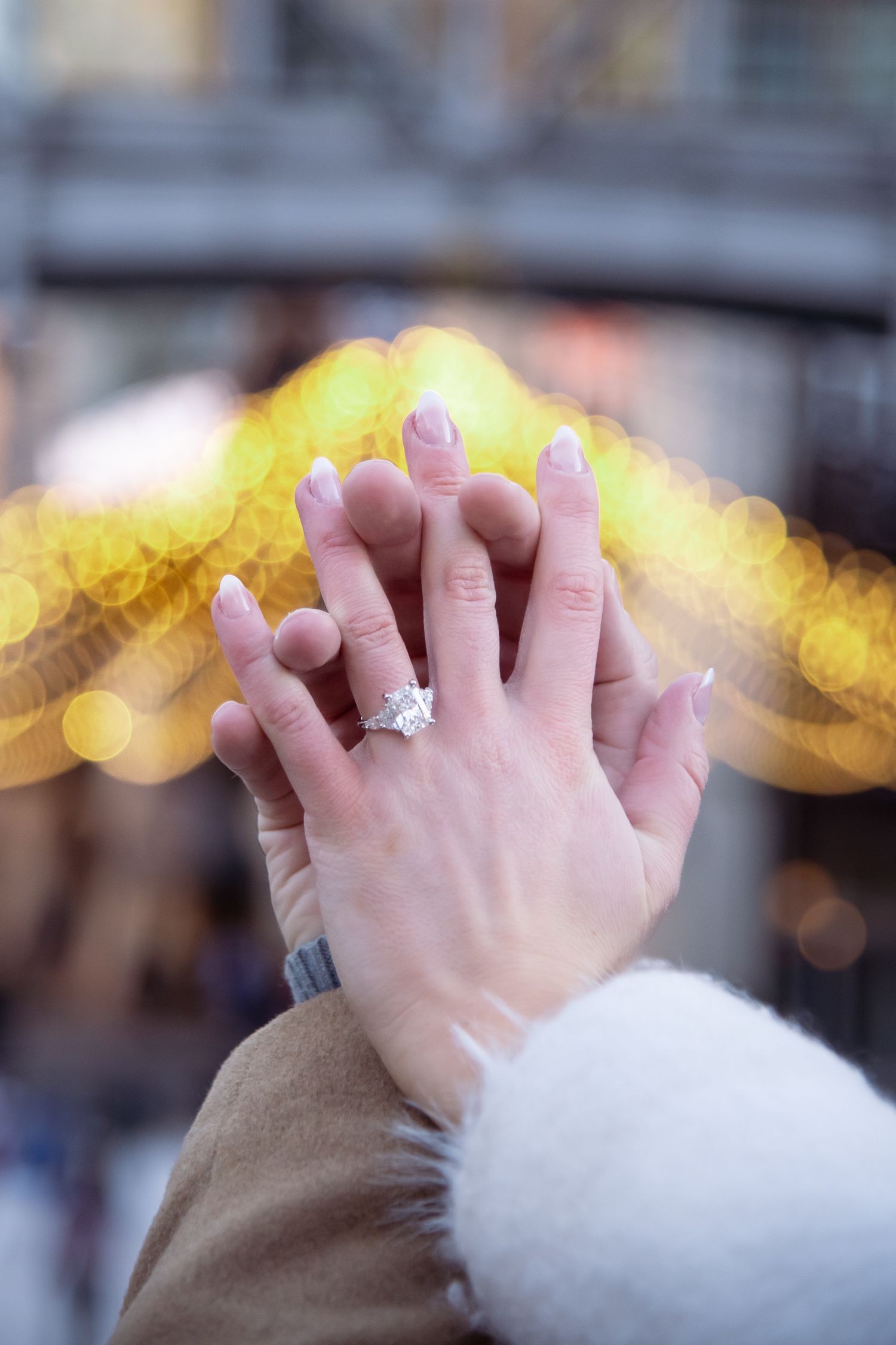 Two hands touching with soft lights in the background and an engagement ring after a winter Vail Colorado proposal