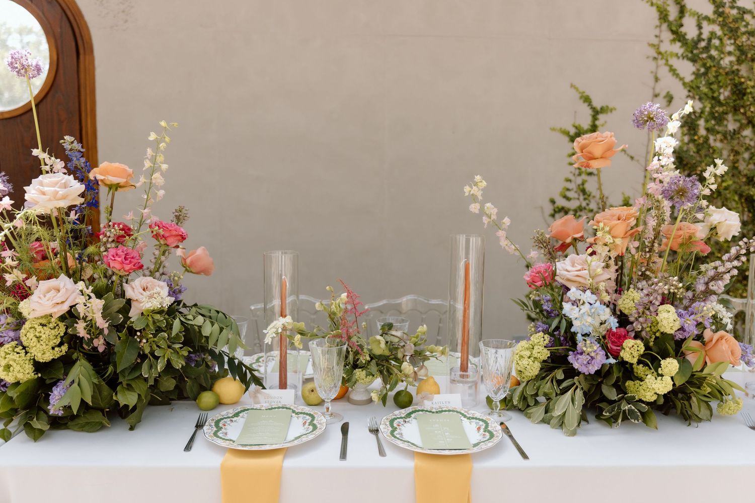 Elegant wedding table settings with pink and peach floral arrangements and gold accents on a white tablecloth.
