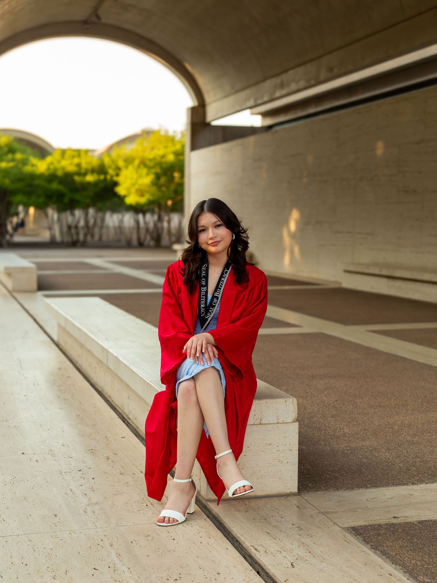 Person in a vibrant red graduation gown sits on concrete steps in an urban setting with soft lighting. Kimbell Art Museum Fort Worth Texas