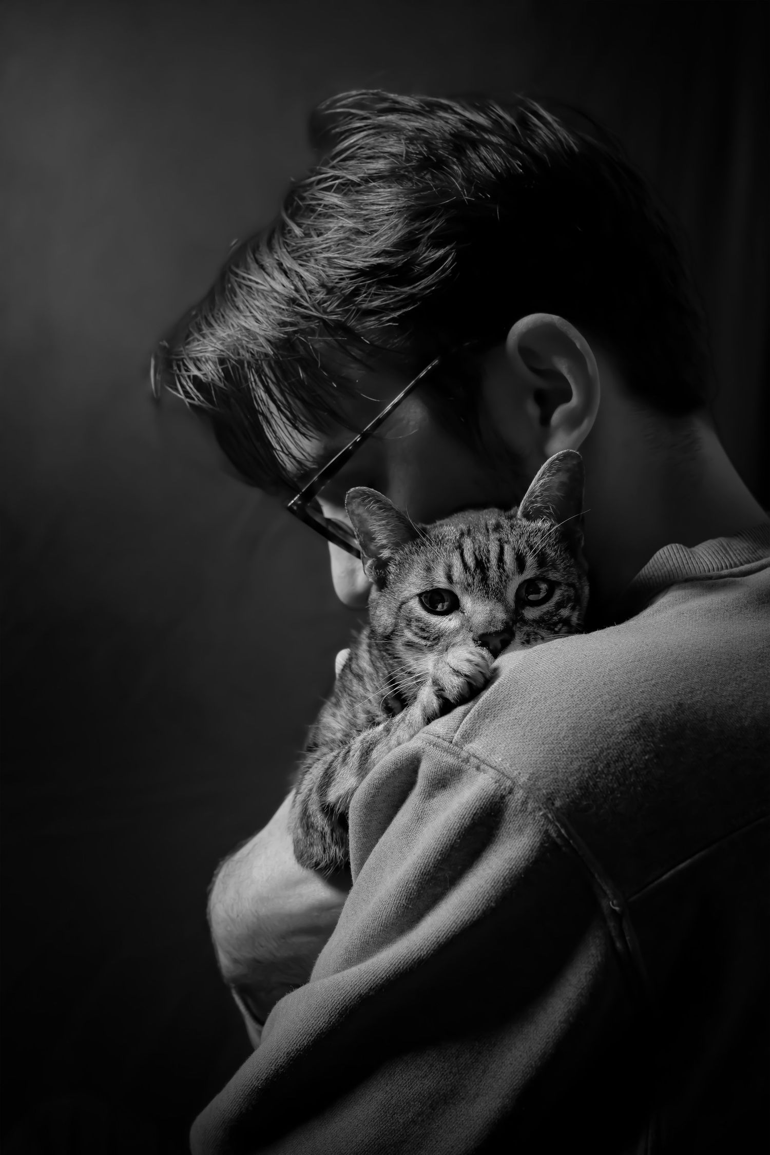 A black and white portrait shows a person in glasses holding a cat close to their face in an intimate moment.