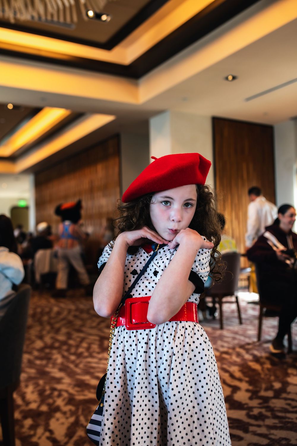 A polka dot dress with red accents is shown in an elegant hotel conference room with warm lighting.