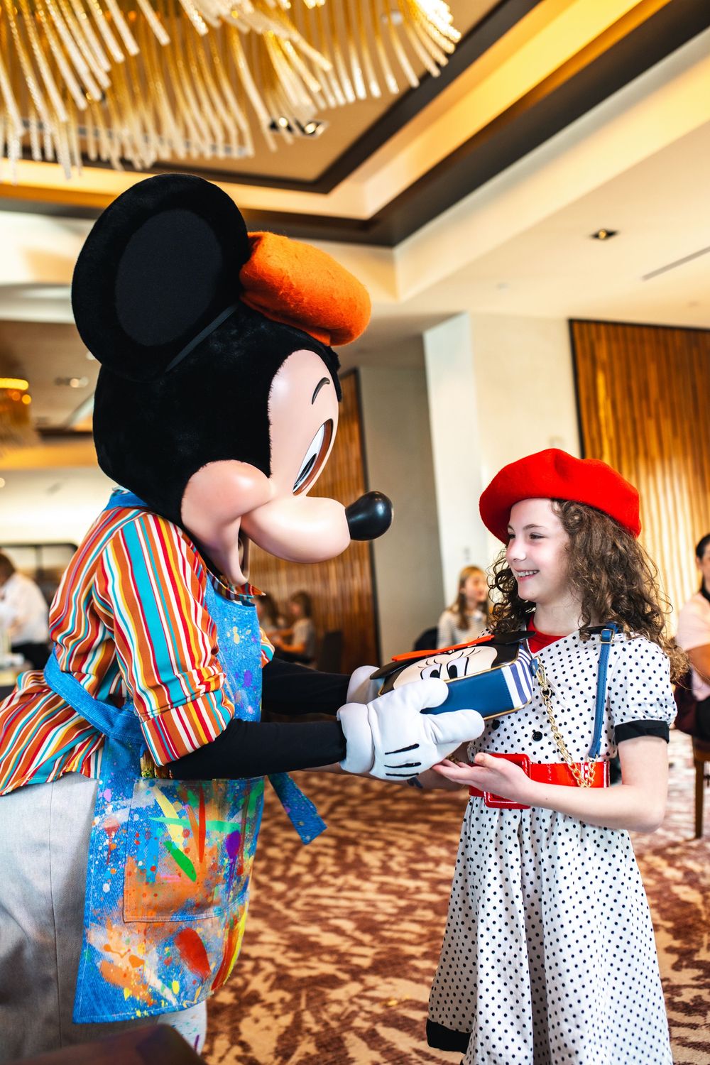 Mickey Mouse character interacts with attendees in a carpeted hotel conference room.