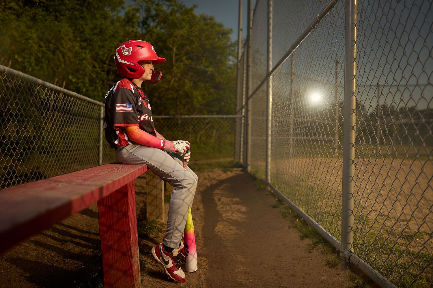 A young baseball player in a black jersey and PM cap poses with their glove in a dramatic dark studio portrait series.