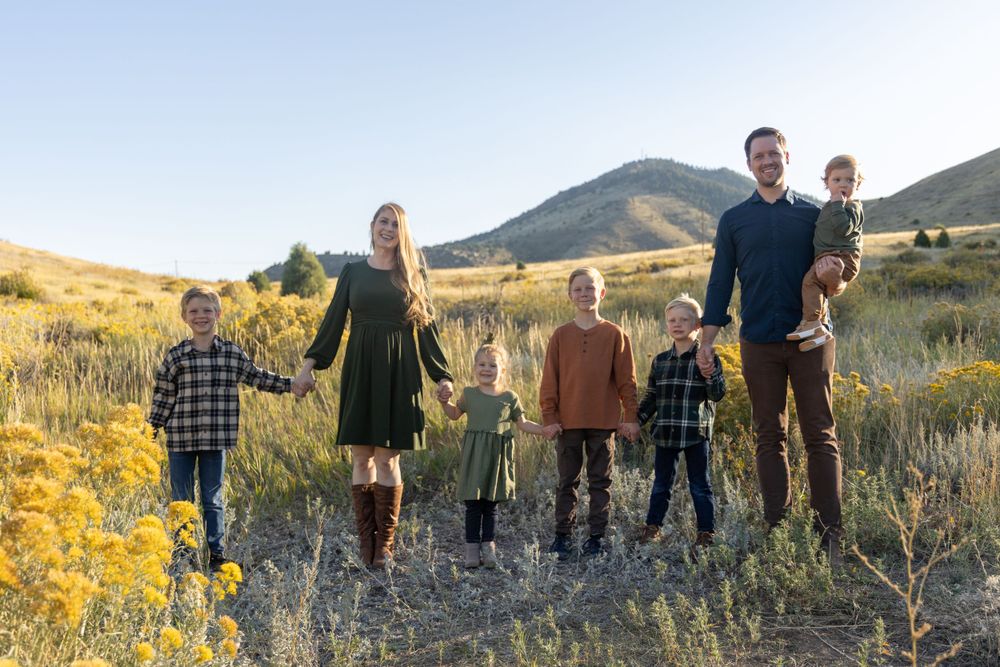A family stands together in a mountain meadow during golden hour with tall grass and wildflowers.