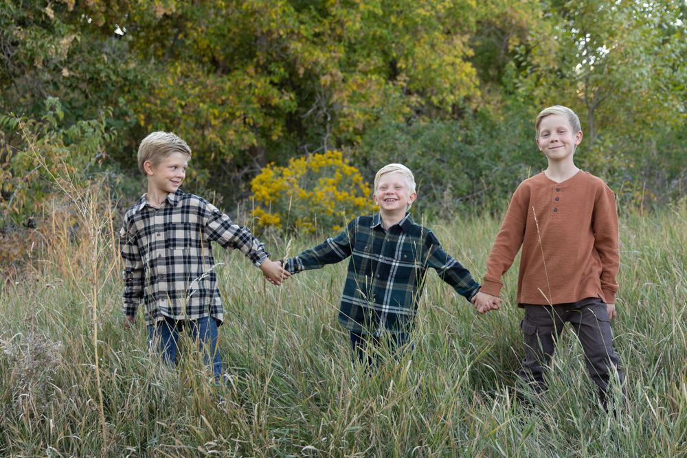 Three children hold hands while playing in tall grass on an autumn day.