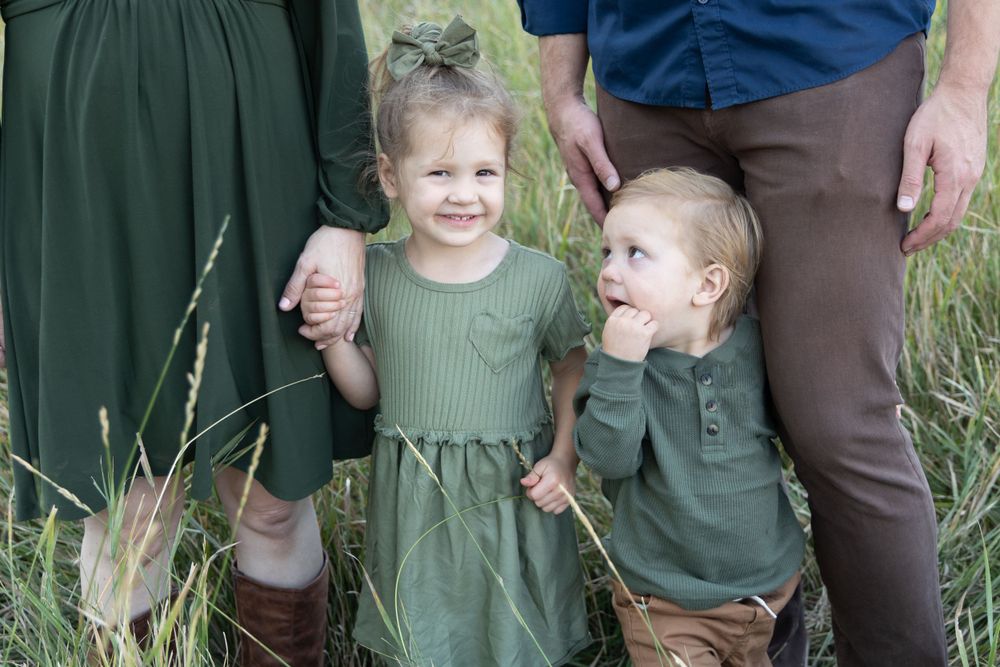 Two small children in matching green outfits share a laugh together in tall grass.