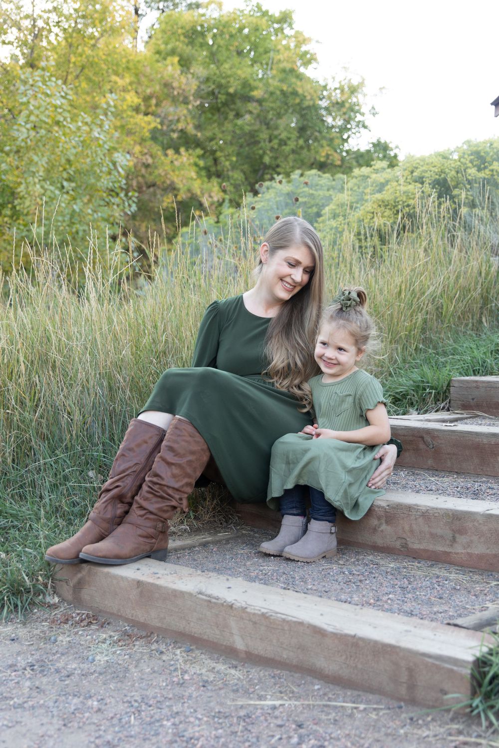 A sweet moment captured on outdoor steps with matching green dresses and natural surroundings.