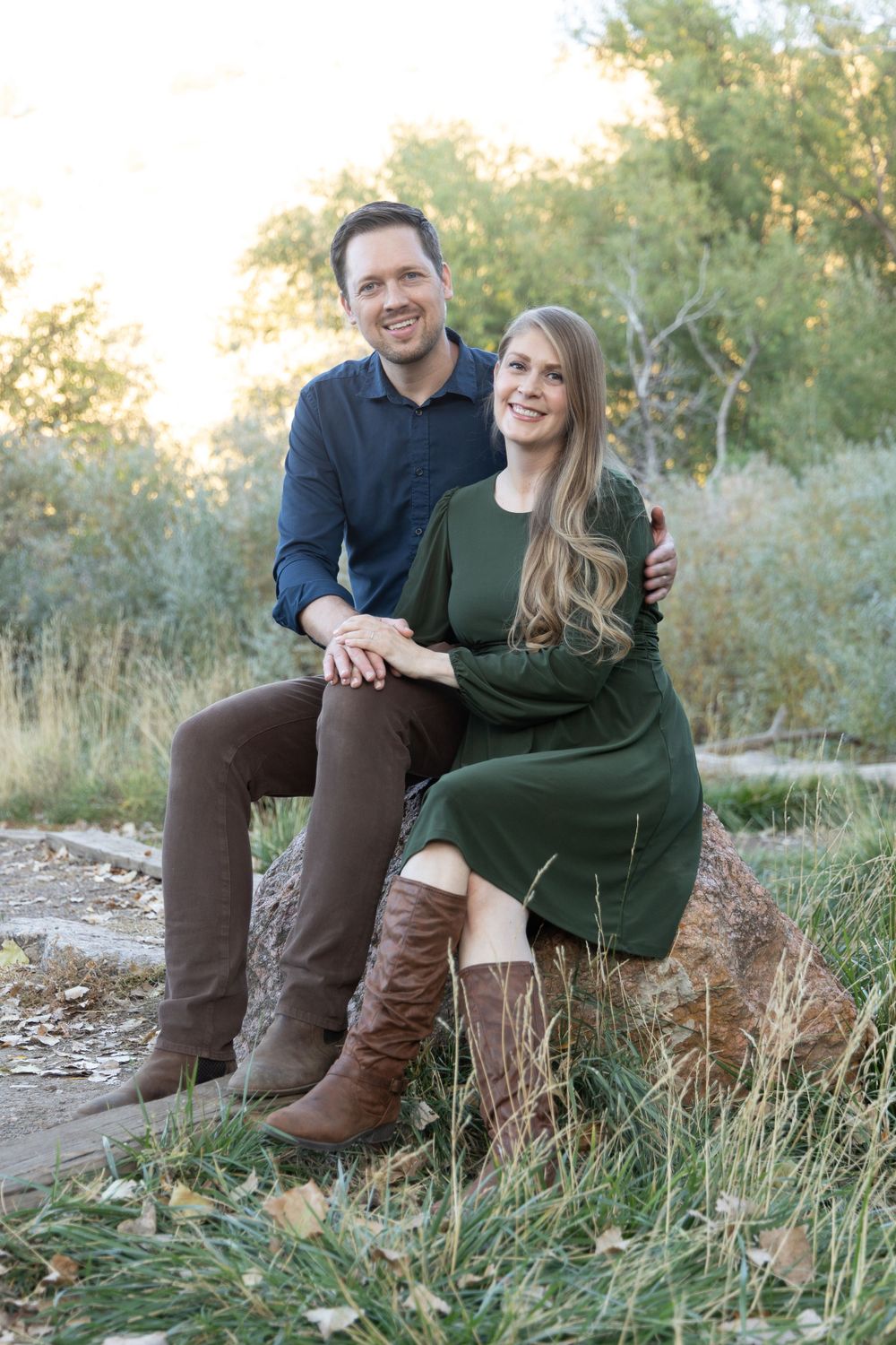A couple sits together on a rocky ledge wearing coordinated outfits in a natural setting.