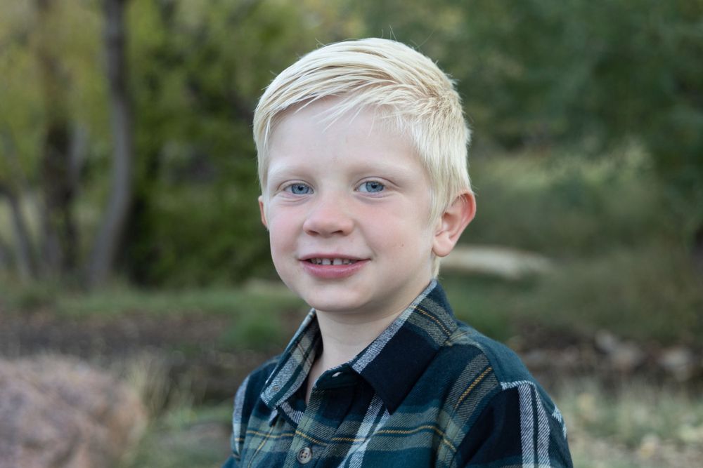 Outdoor portrait showing a cheerful smile wearing a plaid button-down shirt against a natural blurred background.